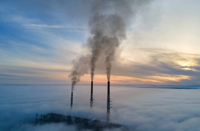 Aerial view of coal power plant high pipes with black smoke moving up polluting atmosphere at sunset.